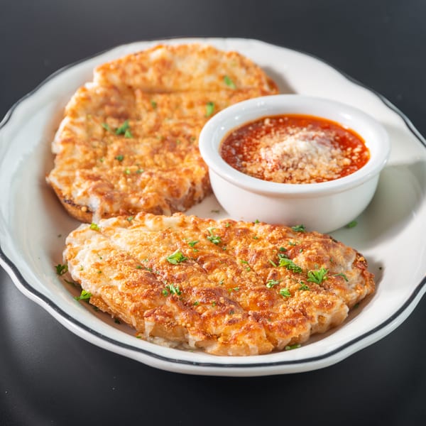 Two golden-brown cheese bread slices with parsley, served with a side of marinara sauce on a white plate.