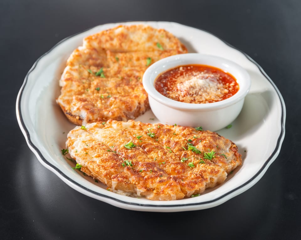 Two golden-brown cheese bread slices with parsley, served with a side of marinara sauce on a white plate.
