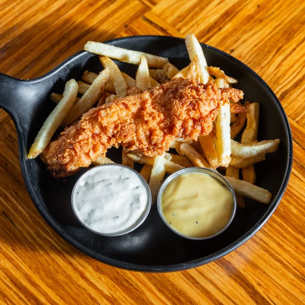 Crispy fried chicken tender and french fries in a black skillet with two dipping sauces.