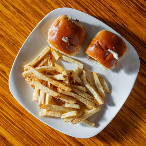 Two sliders with toothpicks and a pile of french fries on a white plate on a wooden table.