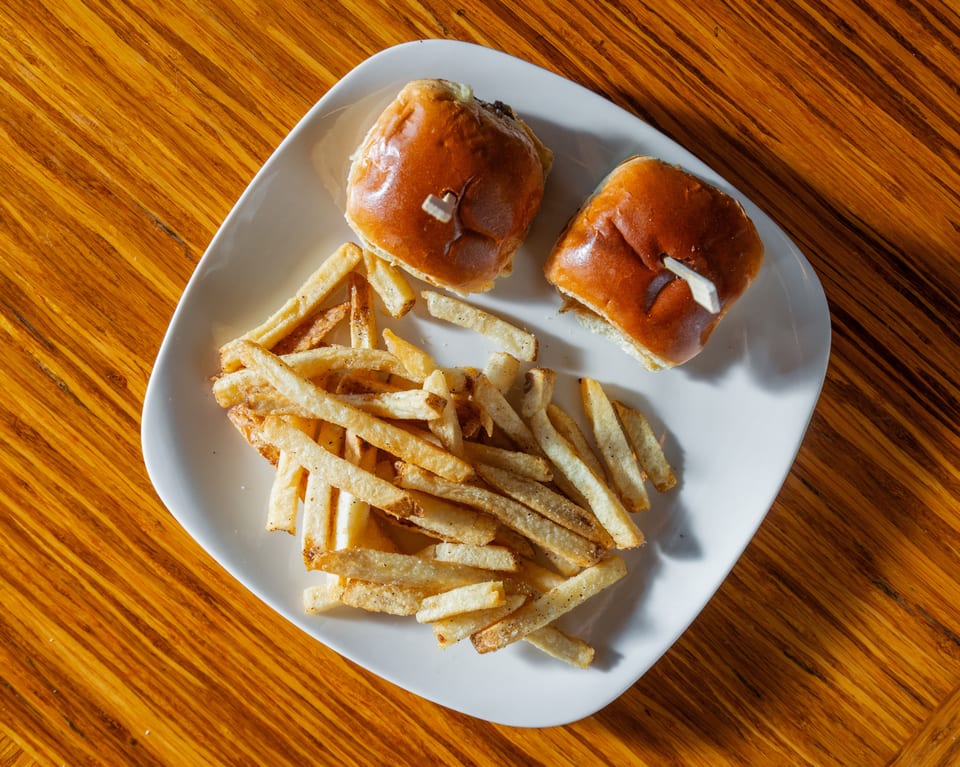 Two sliders with toothpicks and a pile of french fries on a white plate on a wooden table.