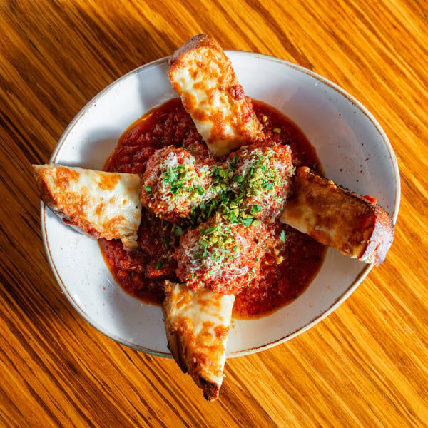 Meatballs in red sauce with melted cheese breadsticks and green garnish on a wooden table.