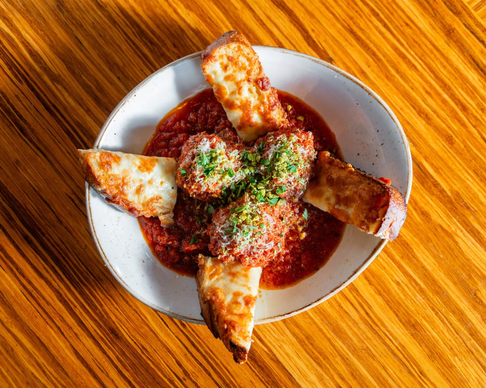 Meatballs in red sauce with melted cheese breadsticks and green garnish on a wooden table.