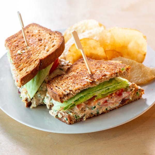 Two halves of a chicken salad sandwich on toasted bread with lettuce, tomato, and potato chips.