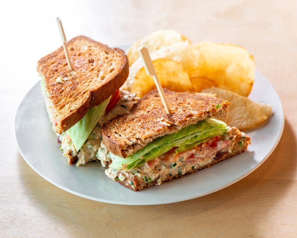 Two halves of a chicken salad sandwich on toasted bread with lettuce, tomato, and potato chips.