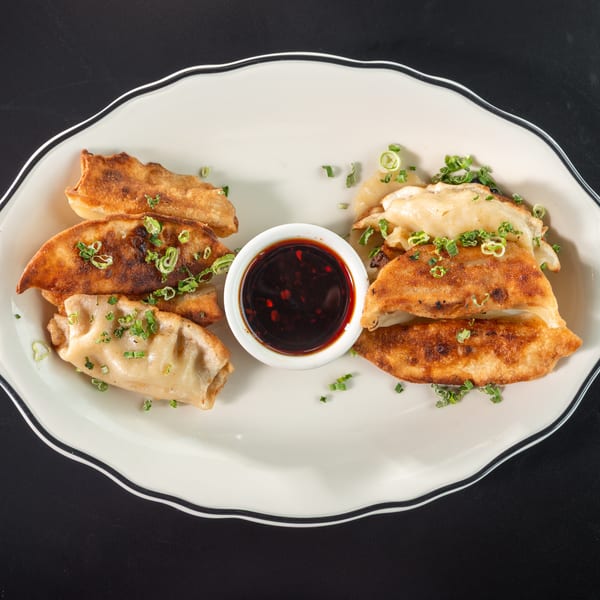 Pan-fried dumplings with crispy edges and green onion garnish, served with a dark dipping sauce.