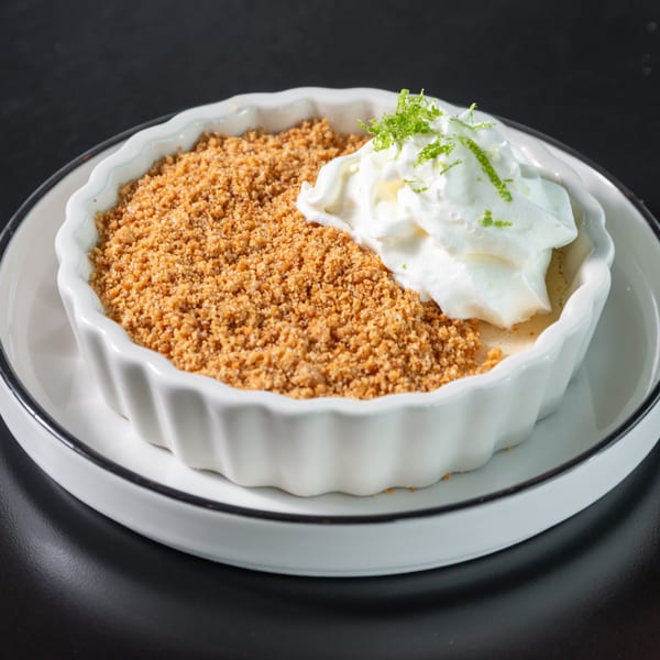 Key lime pie in a white ramekin, topped with whipped cream and lime zest.