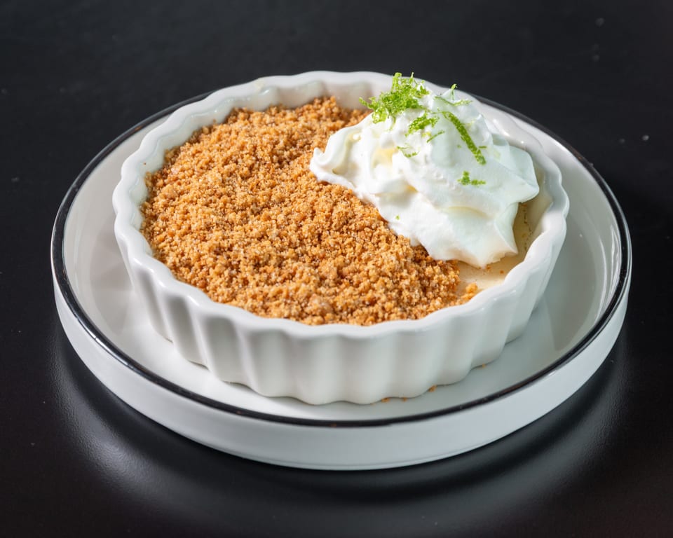 Key lime pie in a white ramekin, topped with whipped cream and lime zest.