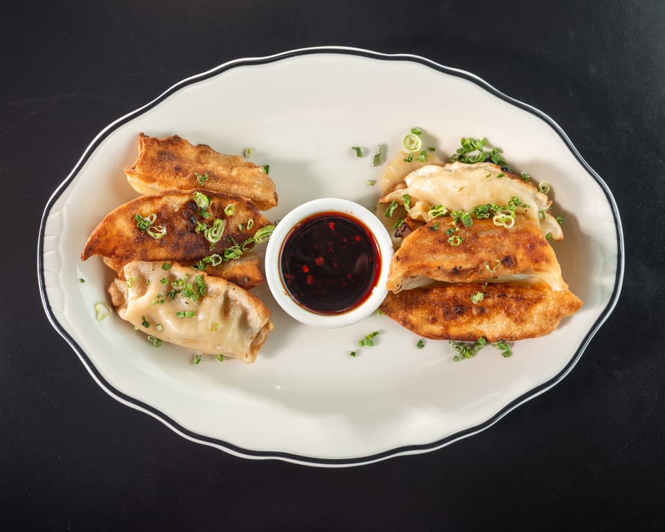 Pan-fried dumplings with crispy edges and green onions, served with a dark dipping sauce.