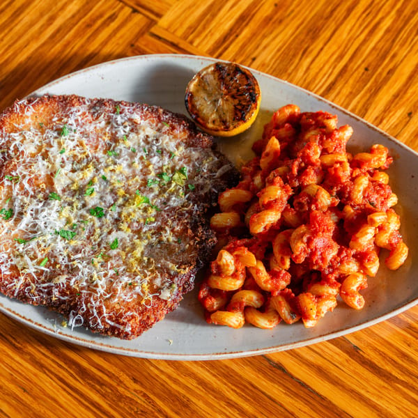 Crispy breaded cutlet topped with cheese and herbs, served with pasta in red sauce and a grilled lemon.
