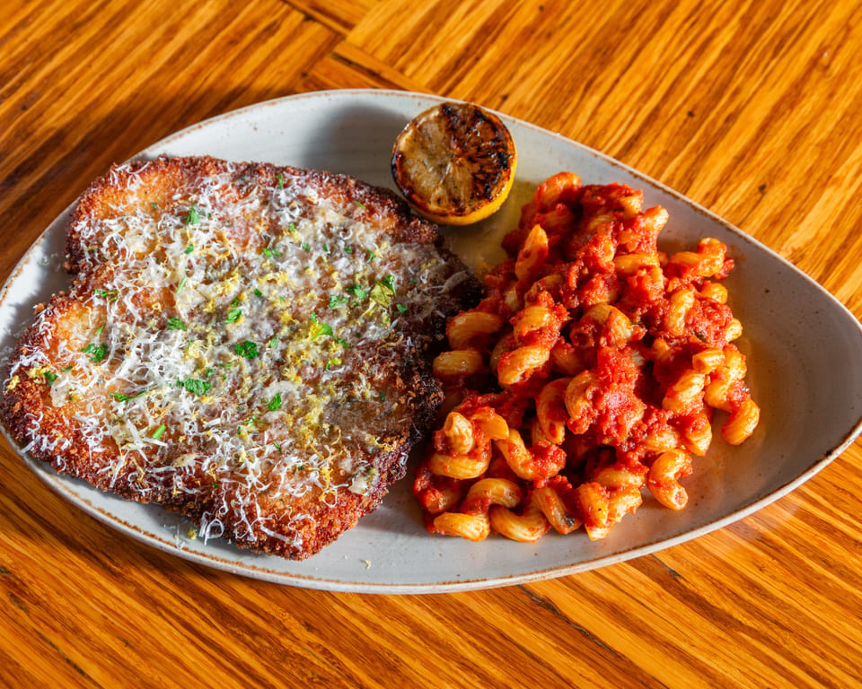 Crispy breaded cutlet topped with cheese and herbs, served with pasta in red sauce and a grilled lemon.