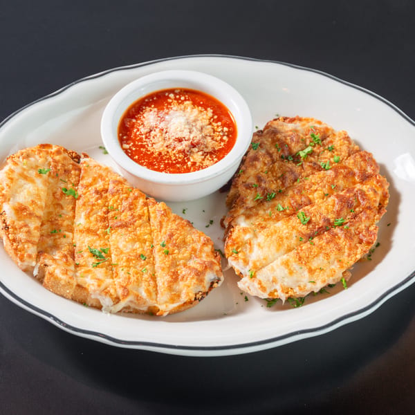 Two pieces of golden-brown garlic bread with melted cheese and parsley, served with a side of marinara sauce.