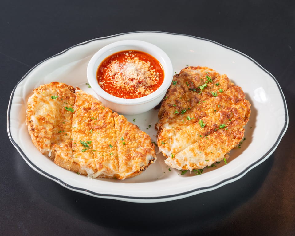 Two pieces of golden-brown garlic bread with melted cheese and parsley, served with a side of marinara sauce.
