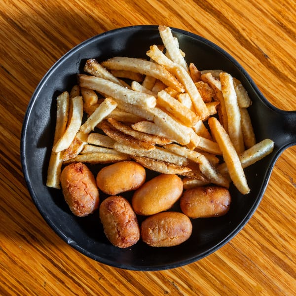 Golden french fries and several mini corn dogs in a black serving dish on a wooden table.