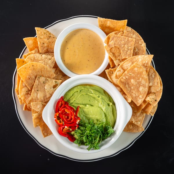 A plate of tortilla chips with bowls of guacamole, queso, and sliced red peppers.