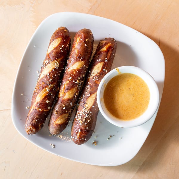 Three pretzel sticks with everything bagel seasoning and a side of cheese dipping sauce.