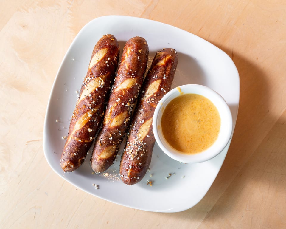 Three pretzel sticks with everything bagel seasoning and a side of cheese dipping sauce.