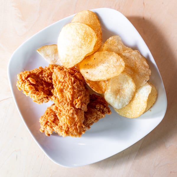 Crispy fried chicken tenders and golden potato chips served on a white plate on a wooden table.