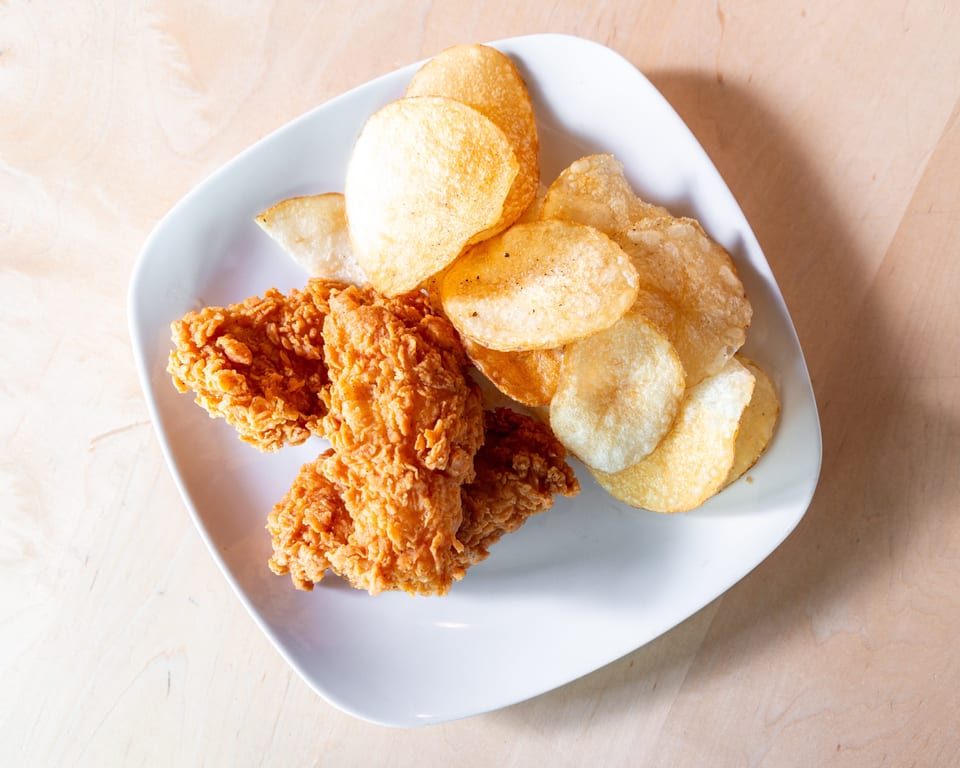 Crispy fried chicken tenders and golden potato chips served on a white plate on a wooden table.
