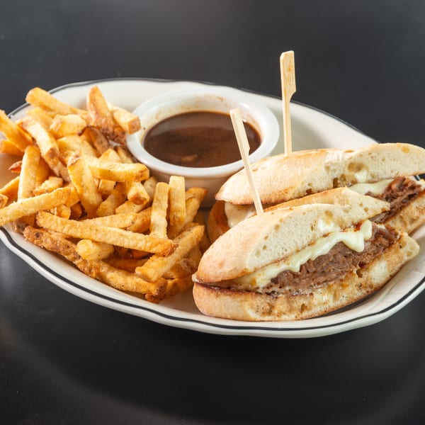 French dip sandwiches with melted cheese, a side of fries, and a small bowl of au jus.