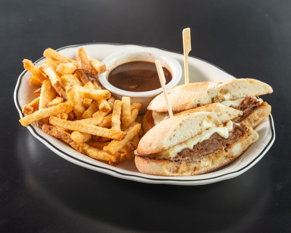 French dip sandwiches with melted cheese, a side of fries, and a small bowl of au jus.